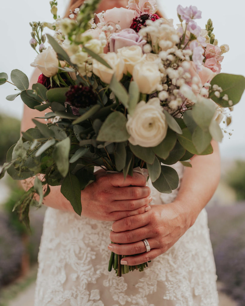 Bride holds her white, purple, and green wedding bouquet 