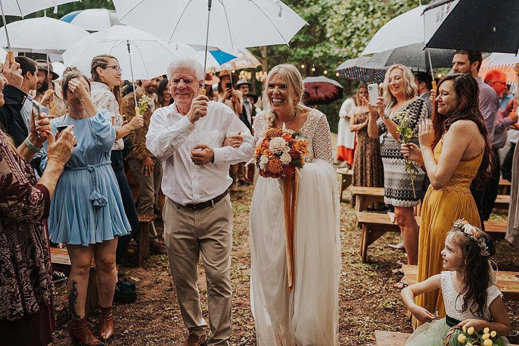 Boho bride walking down the outdoor aisle in Tennessee holding an umbrella