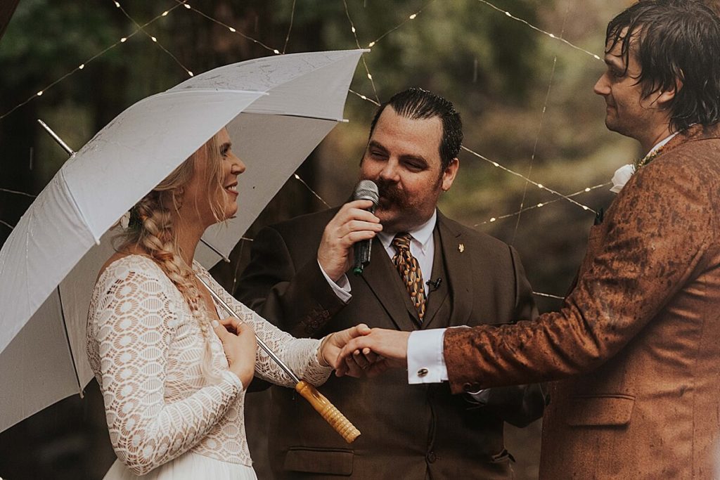 Boho bride and groom at the altar holding an umbrella with their officiant 