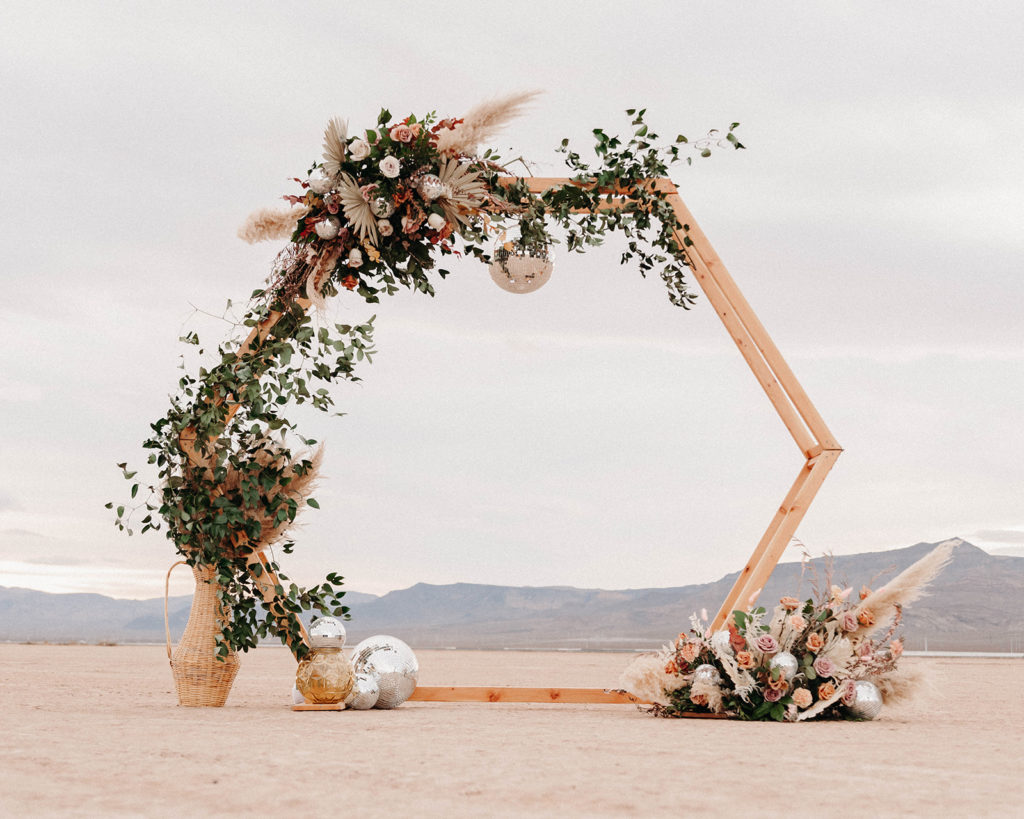 Las Vegas desert elopement ceremony setup with a wooden hexagon arch with flowers and disco balls.