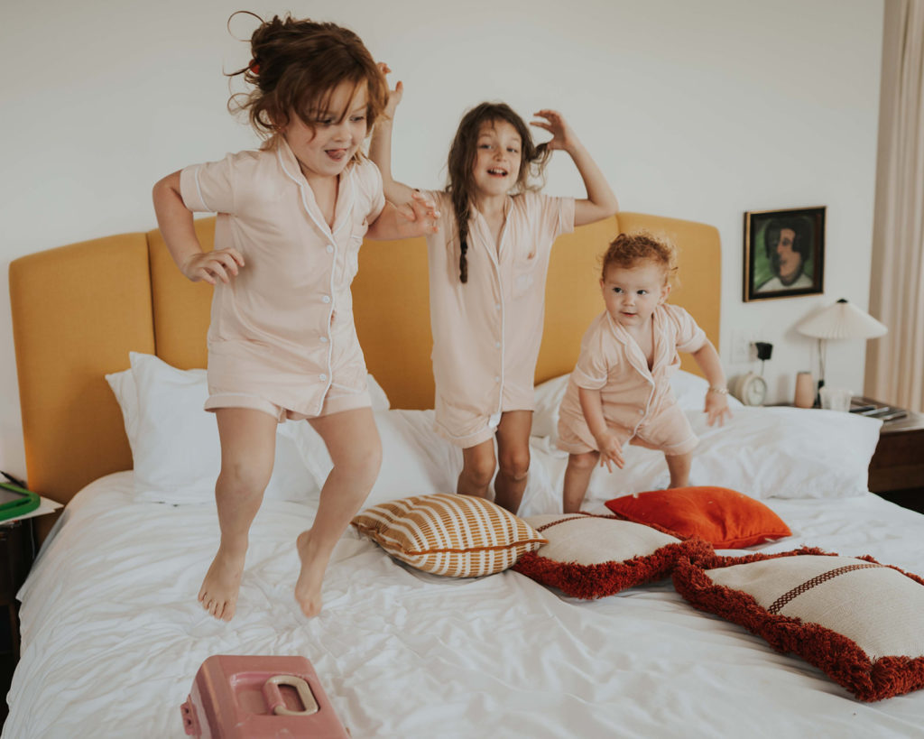 Three little girls in matching pajamas jumping on the bed at the Common House in Chattanooga, Tennessee.