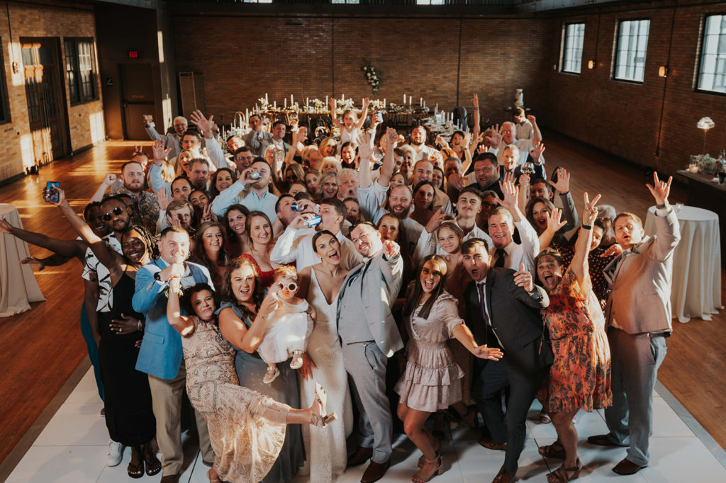 Elevated group wedding photo with everyone holding their hands up.