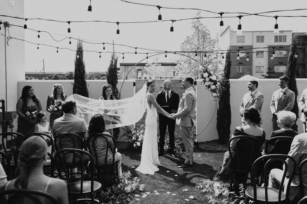 Outdoor summer wedding ceremony at the Common House in Chattanooga, TN featuring a round arch with flowers and hanging string lights.