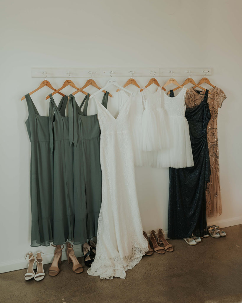 Wedding day detail photo featuring the bride and bridesmaid dresses hanging on wooden hangers. 