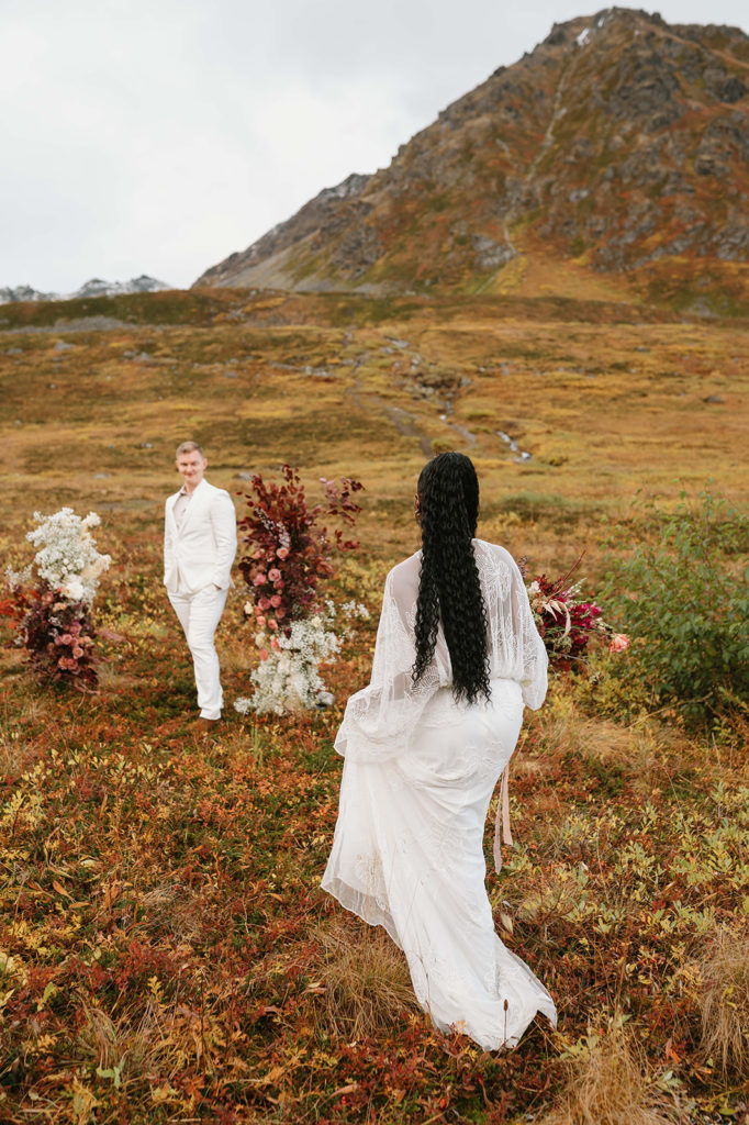 Bride walking towards groom at their outdoor wedding ceremony in Alaska.