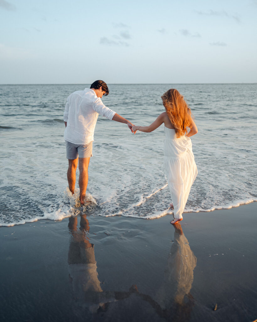 Man leads his fiancé into the ocean during their engagement photos.