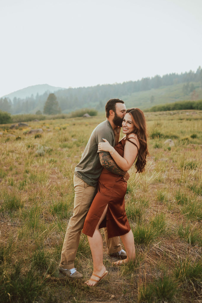 The couple is demonstrating an example of what to wear for your engagement photoshoot. She is wearing a satin, rust colored dress. He is wearing khaki pants and a muted green shirt.