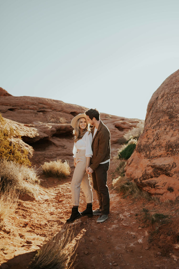 Utah Desert Engagement Photographs. The couple is demonstrating an example of what to wear for your engagement photoshoot.  They are wearing earthy toned colors with layered shirts. The girl is wearing a hat. 