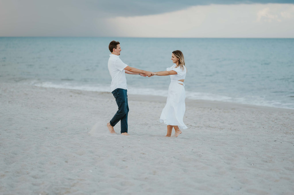Man and woman playing together on the beach while holding hands
