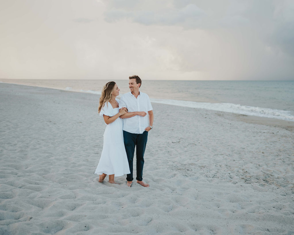 a couple smiles at each other during their beach engagement photographs