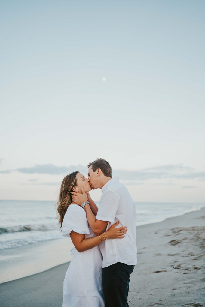 man and woman share a kiss during their beach engagement photographs