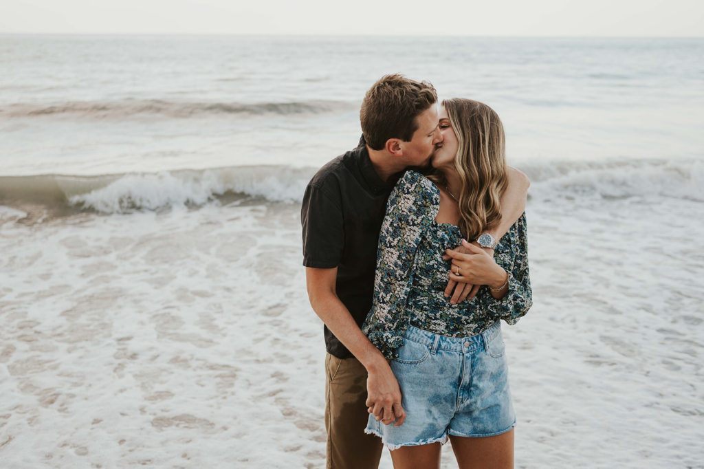 Man and woman kiss each other on the beach during their beach engagement photos 