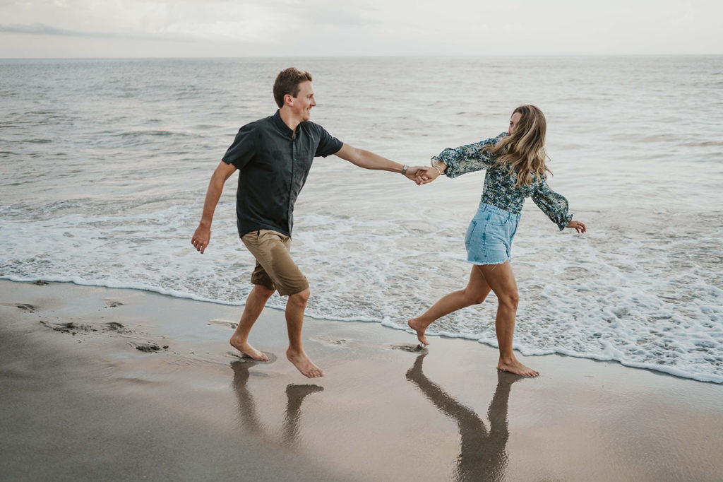 Woman playfully pulls man by the hand along the ocean shoreline