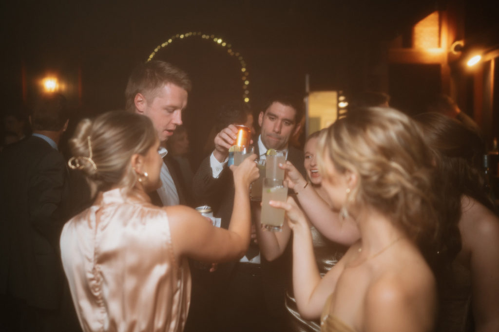 Wedding guests clink their cocktail glasses together to celebrate 