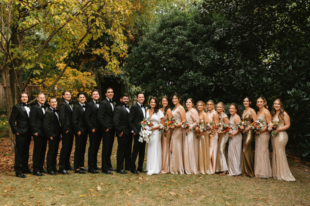 Full wedding party stands in a line and smiles at camera