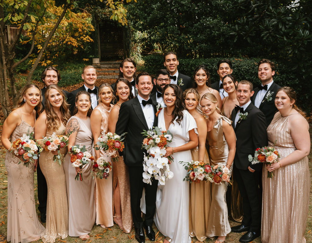 Full wedding party gathers into a bunch smiles at camera