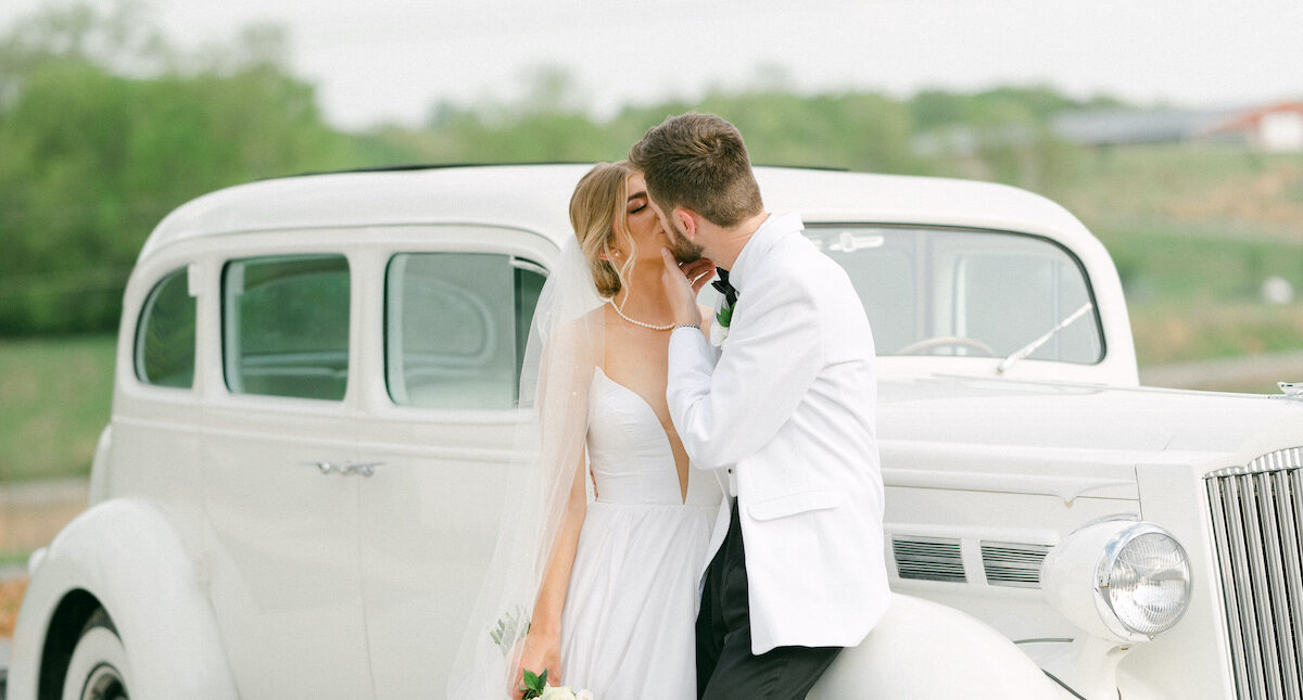 Bride and groom standing by vintage white car.