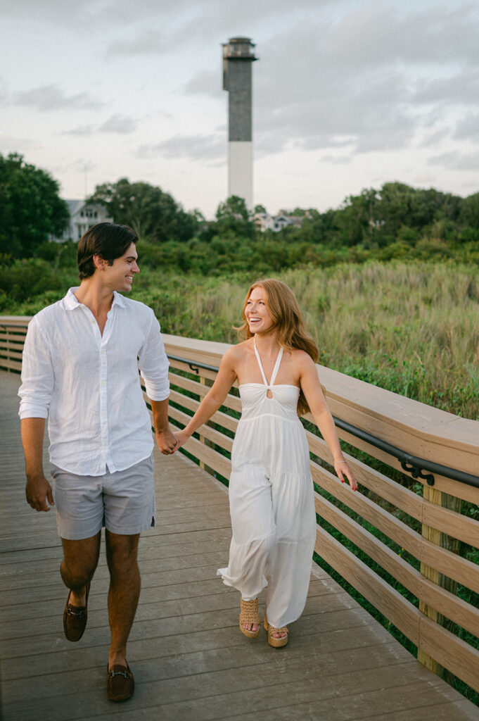 Candid engagement photo at Sullivan's Island with Morris Island Lighthouse in the background.