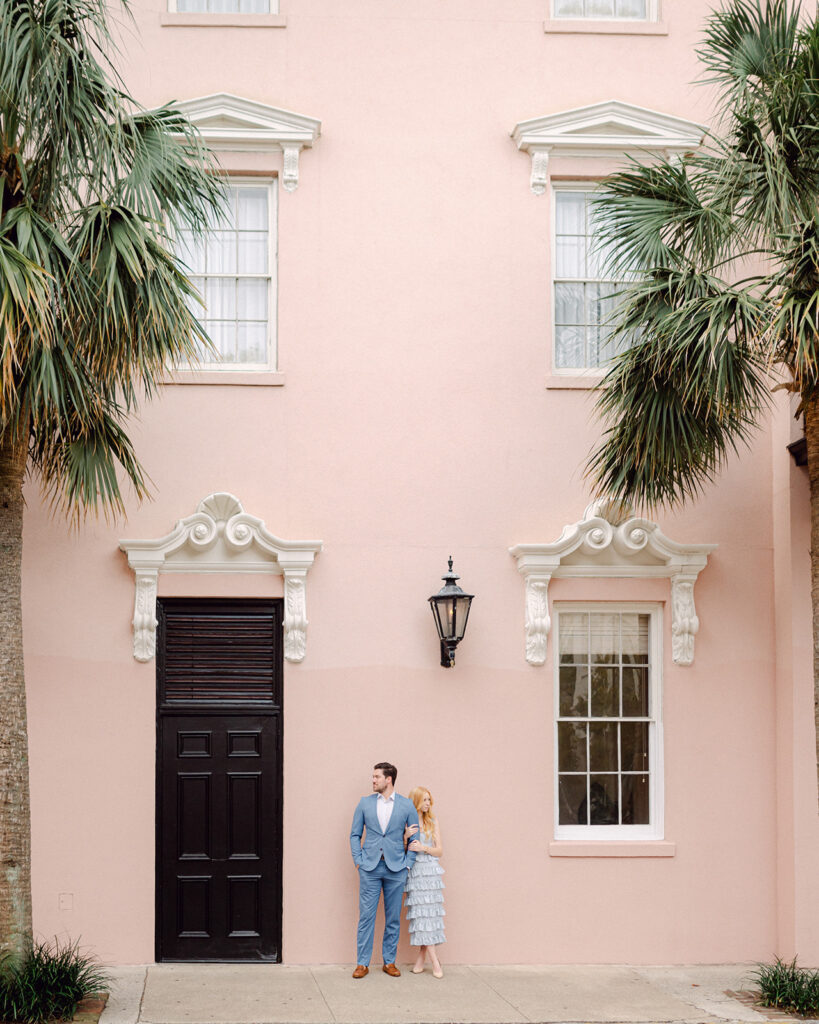 Couple posing against a pastel pink building in the French Quarter in Downtown Charleston.