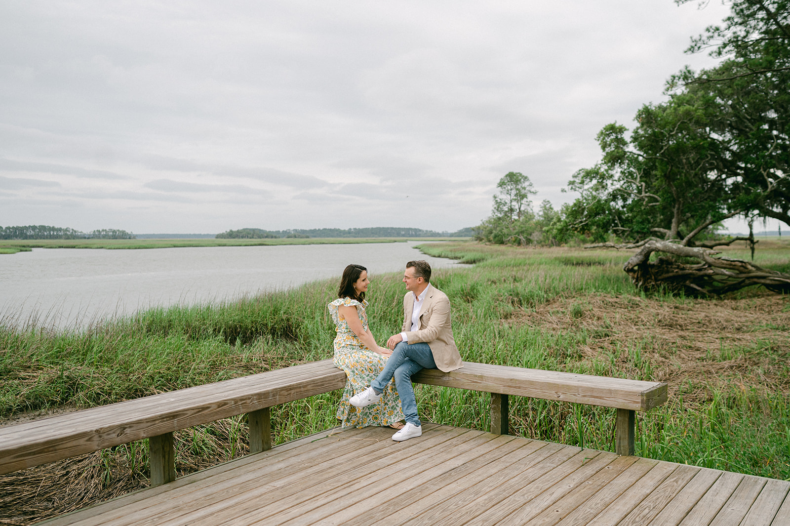 Couple sitting on a wooden bench near a river marsh in Palmetto Bluff, Bluffton, South Carolina. 