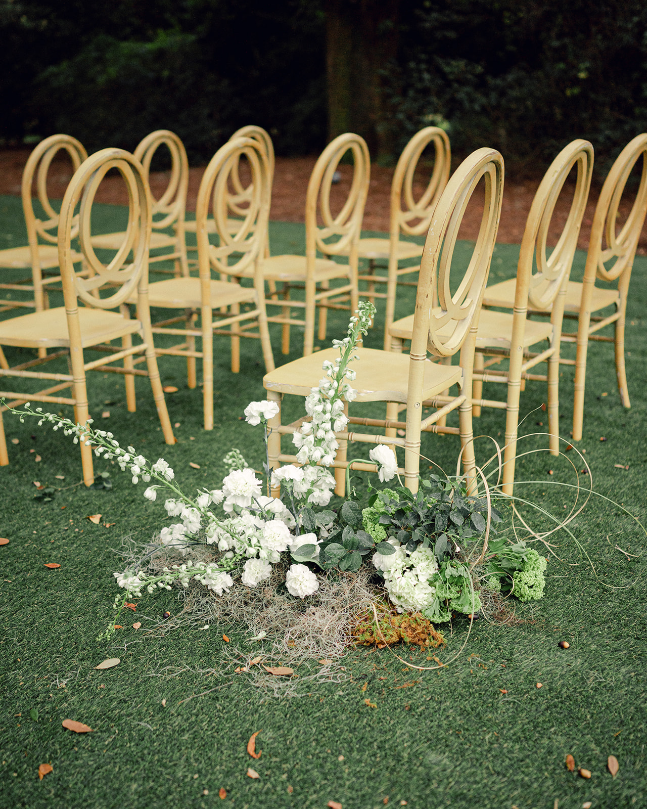 Modern wooden chairs and large floral aisle arrangements featured at an outdoor Legare Waring House wedding ceremony.