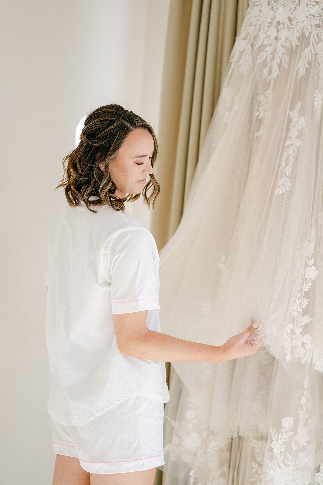 Bride wearing white short pajamas holding her wedding gown. 