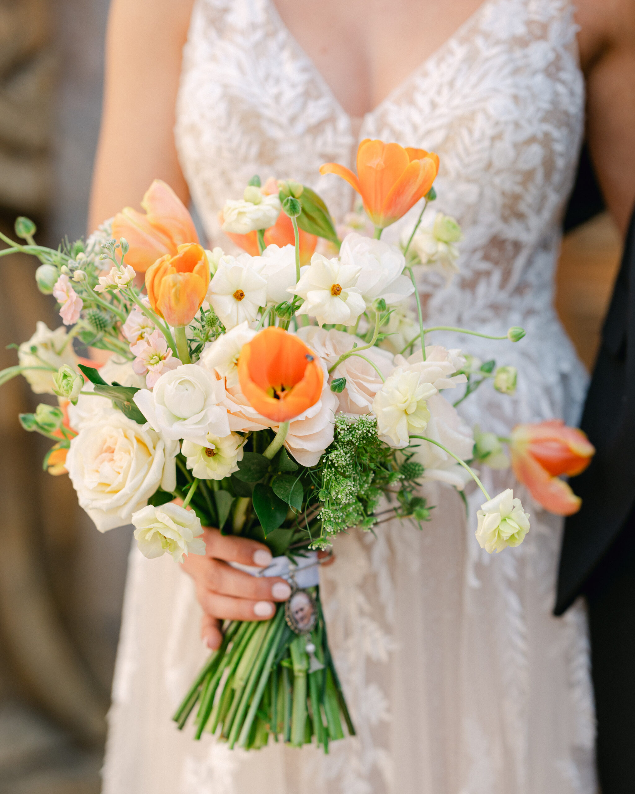 Bride holding her white, orange, and light pink bouquet of flowers on her wedding day. 