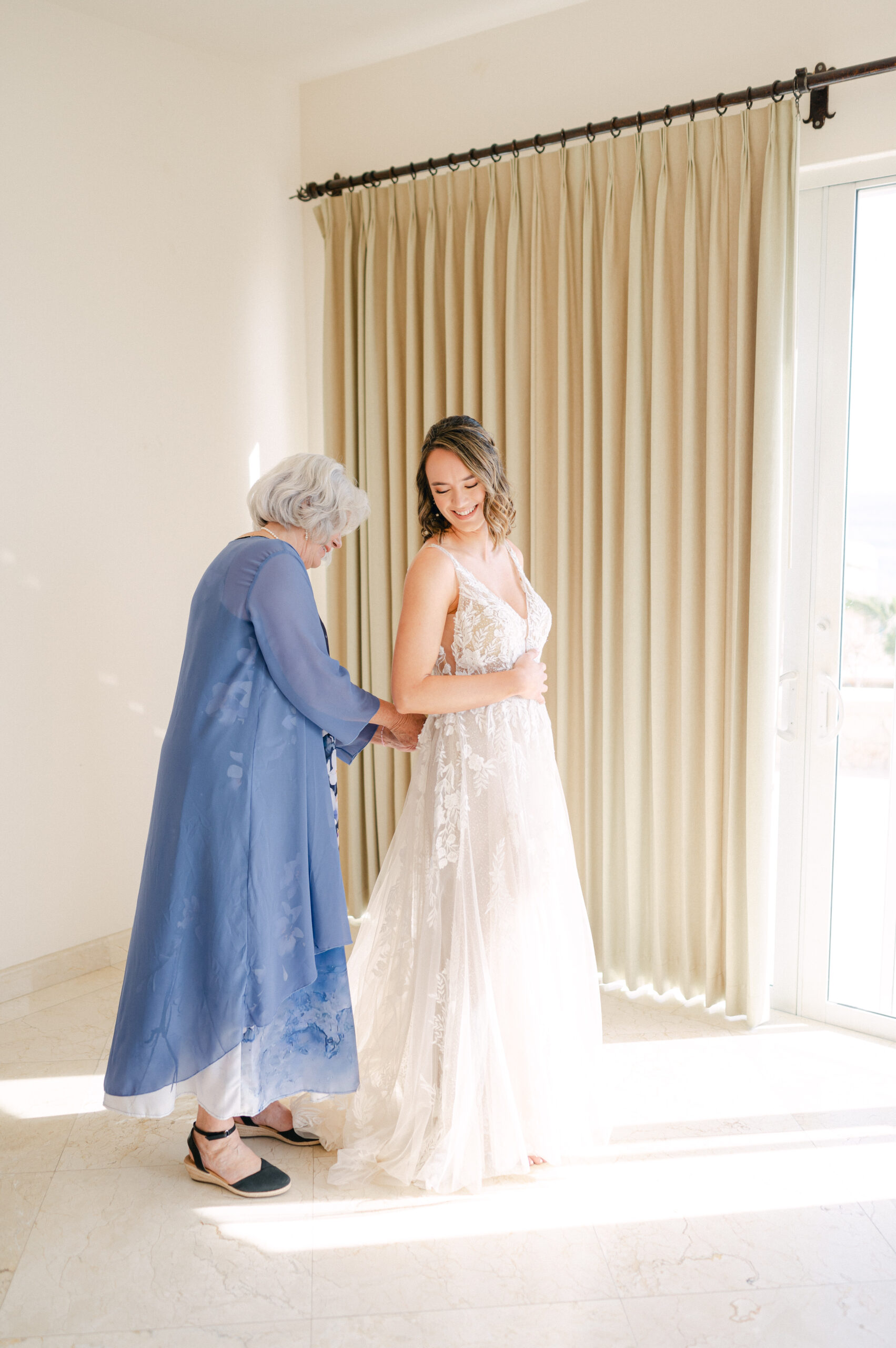 Mother of the bride helping her daughter into her daughter's wedding dress.