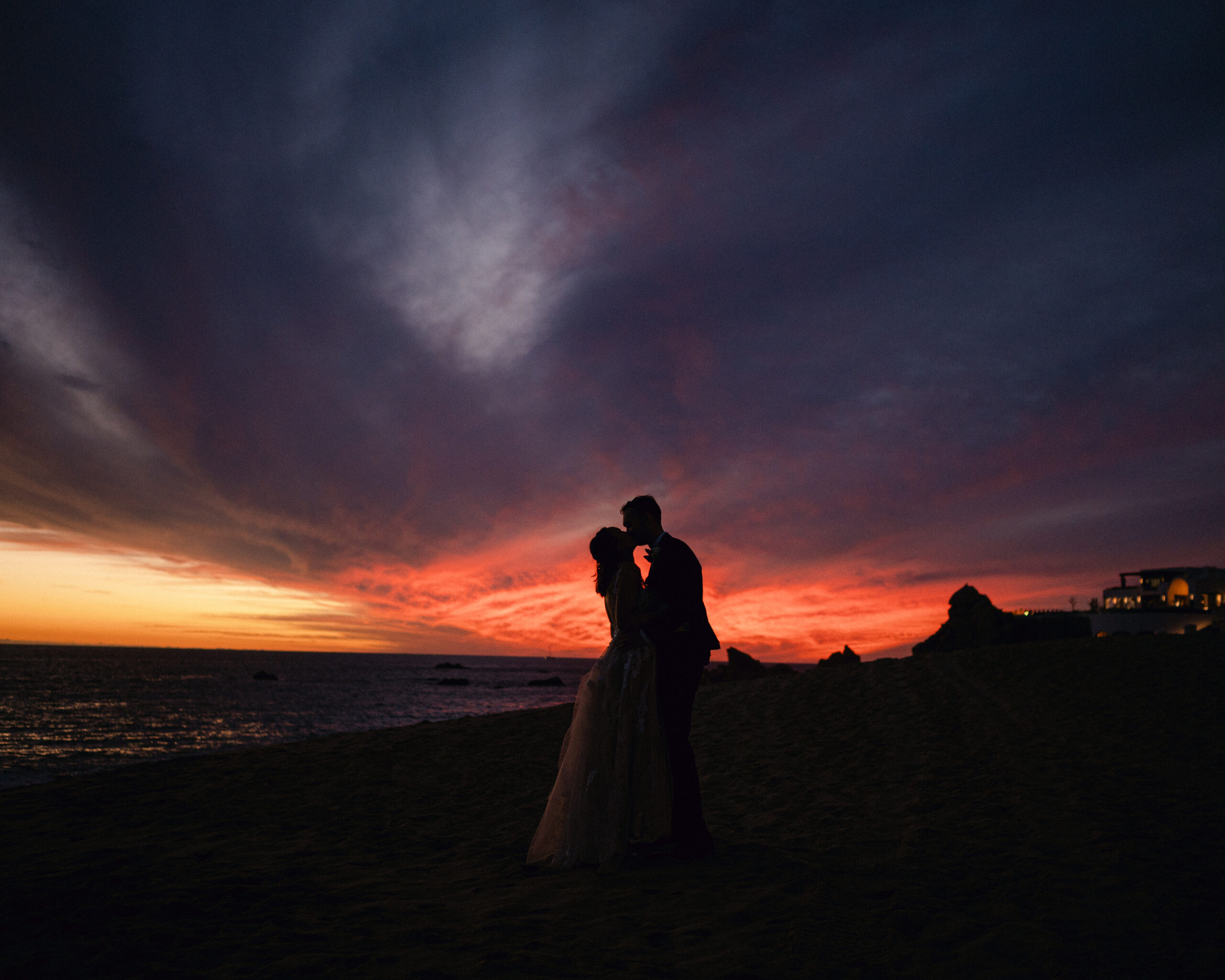 Bride and groom sharing a kiss at sunset on the beach in Cabo. 