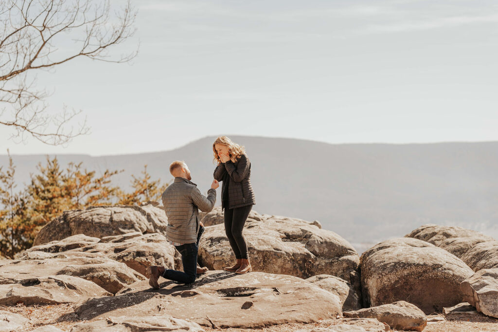 Man on one knee proposing to his girlfriend in the mountains.