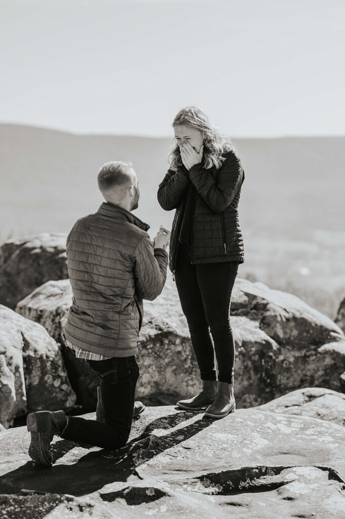 Man kneeling on one knee and holding a ring out for his girlfriend during their engagement proposal.
