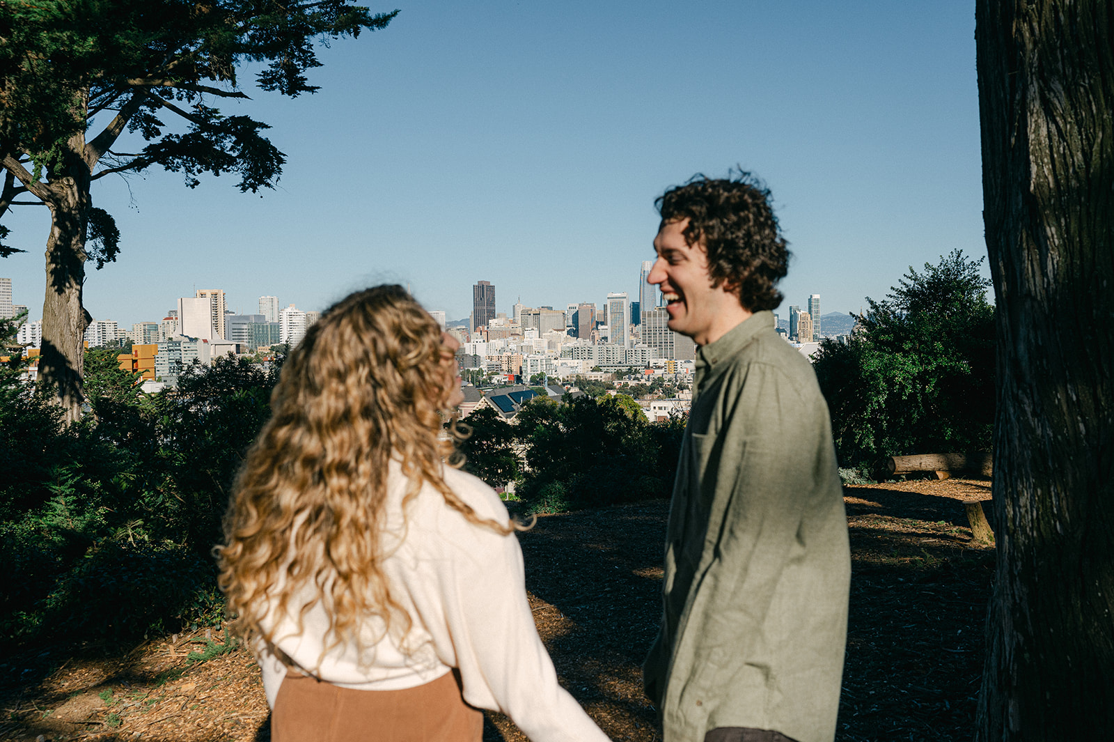 Candid engagement photo at Alamo Square Park in San Francisco with the skyline in the distance.