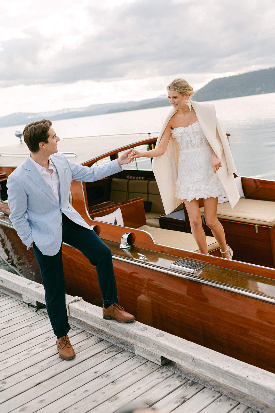 Husband helps his wife step out of their boat onto the dock at Sugar Pine State Park, a Lake Tahoe engagement photo location.