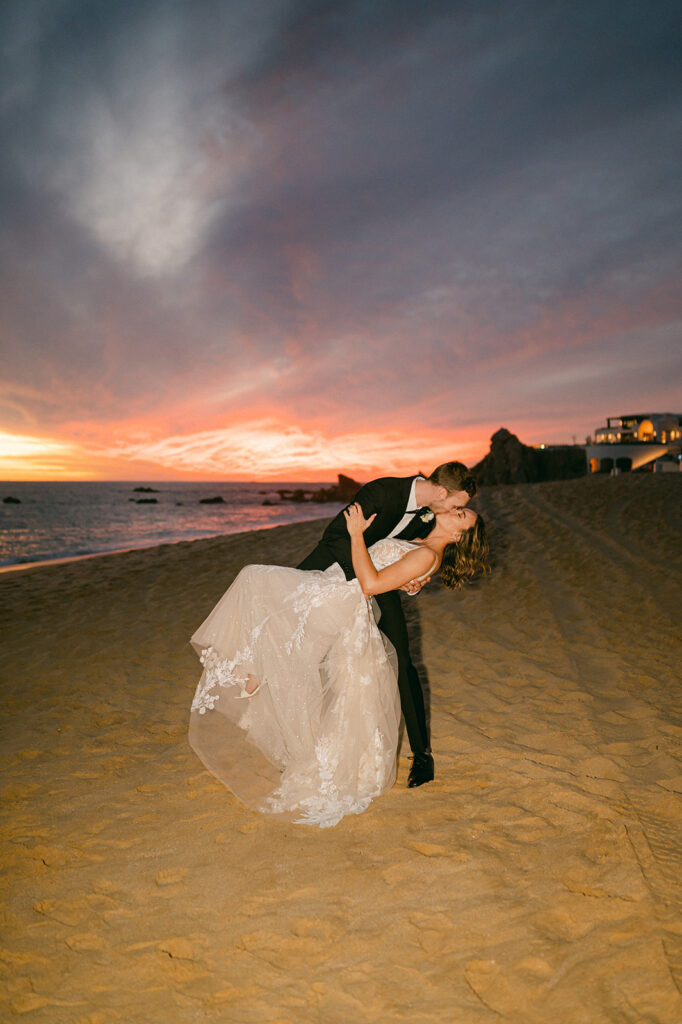 Bride and groom direct flash kissing on the sand in Cabo. 