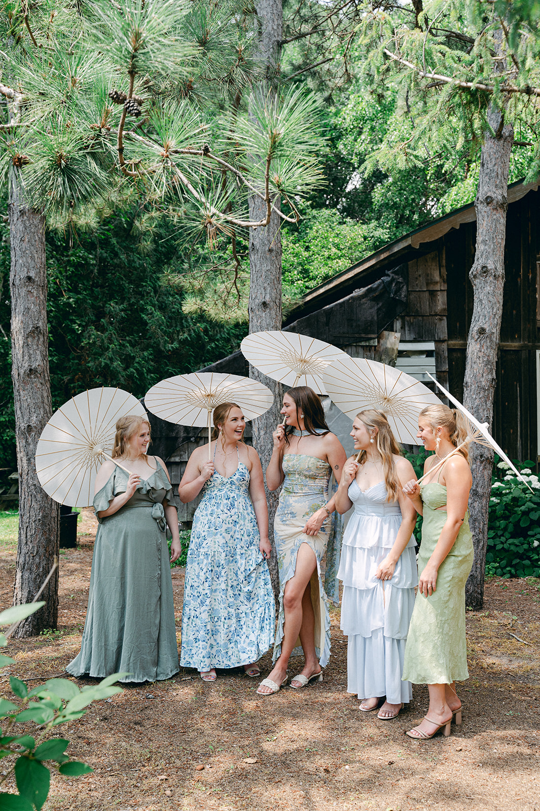 Documentary-style shot of the bridal party gathered in the garden, with  stylish floral dresses and parasol umbrellas. 