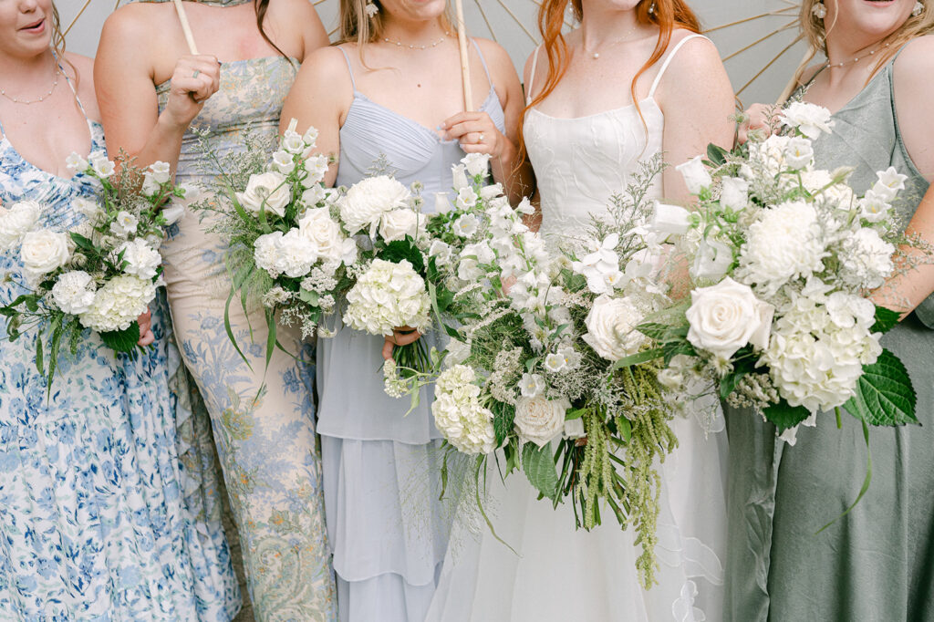 Bridesmaids dressed in blue and green floral patterns, holding their white bouquets.