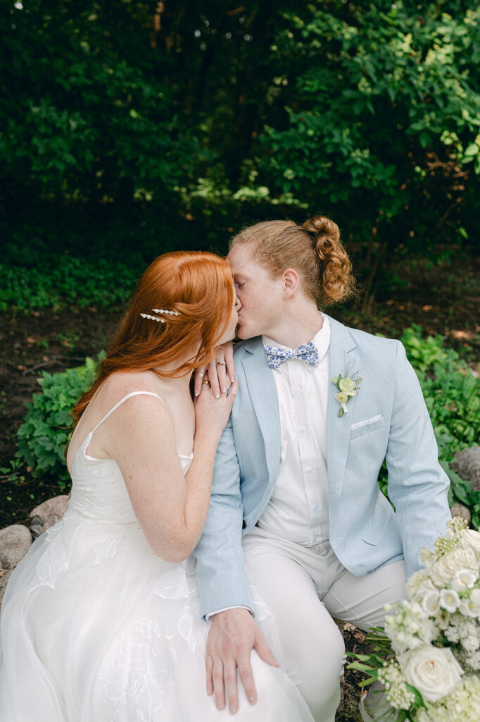 Bride and groom sharing a kiss amidst the lush greenery of their garden party wedding.