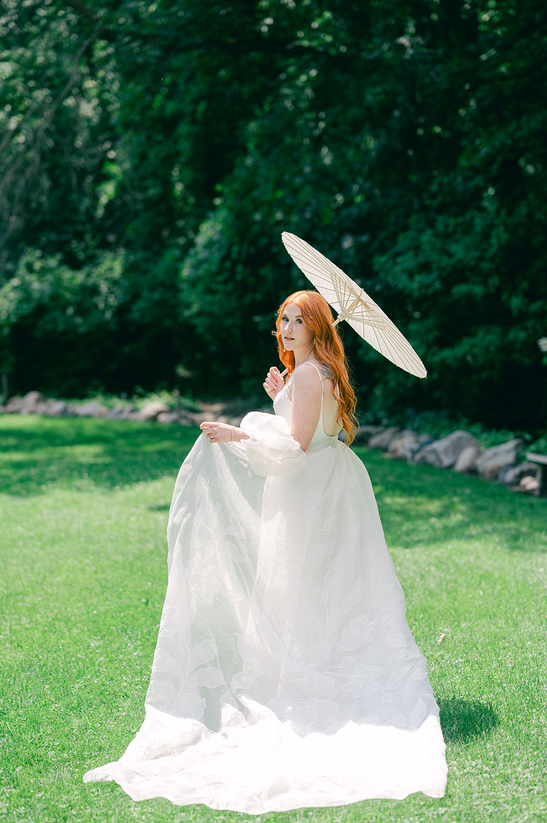 Playful shot of the bride in the garden, twirling with her parasol umbrella, her dress flowing gracefully in the breeze.