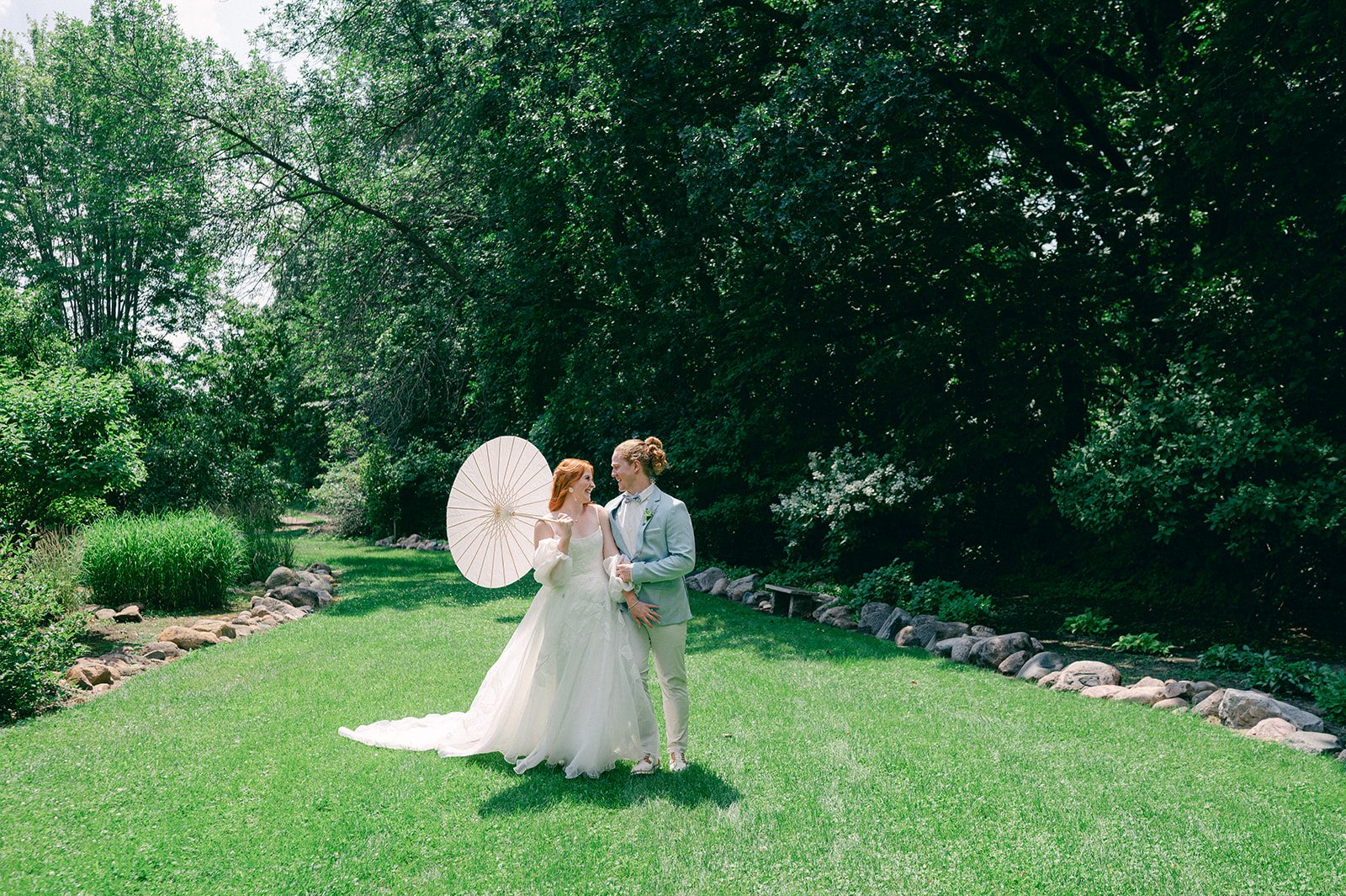 Cinematic bride and groom portrait with a flowing dress and parasol, capturing the playful spirit of her garden party wedding at Battle Lake, MN.