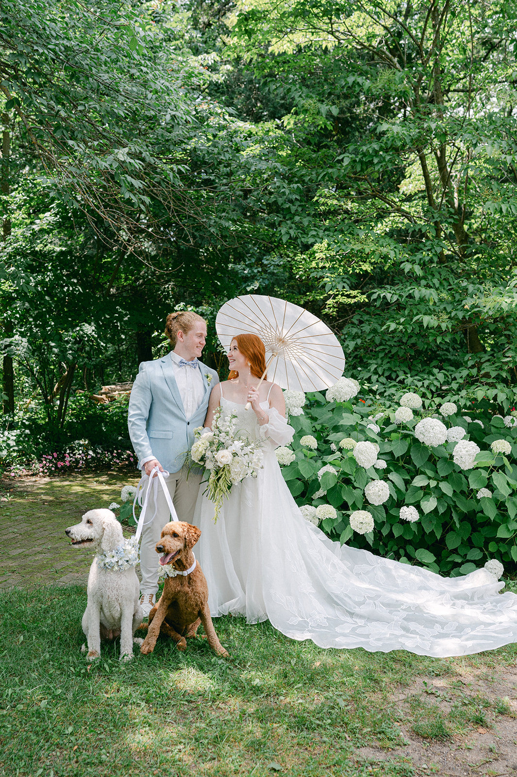 Sweet portrait of the bride and groom surrounded by their two golden doodle dogs in the garden.