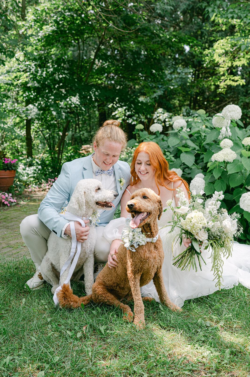 Candid moment of the bride and groom in their garden wedding, playfully posing with their two golden doodle dogs.