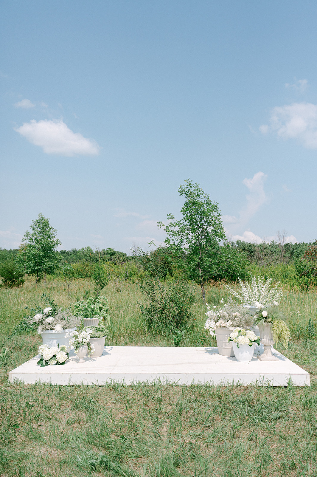 Stunning outdoor garden party wedding setup with a white platform altar surrounded by potted white florals.