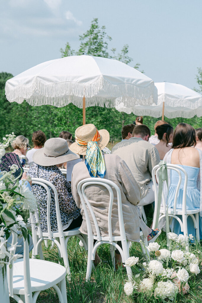 Candid garden wedding ceremony photos of guests sitting in white chairs under large white umbrellas. 