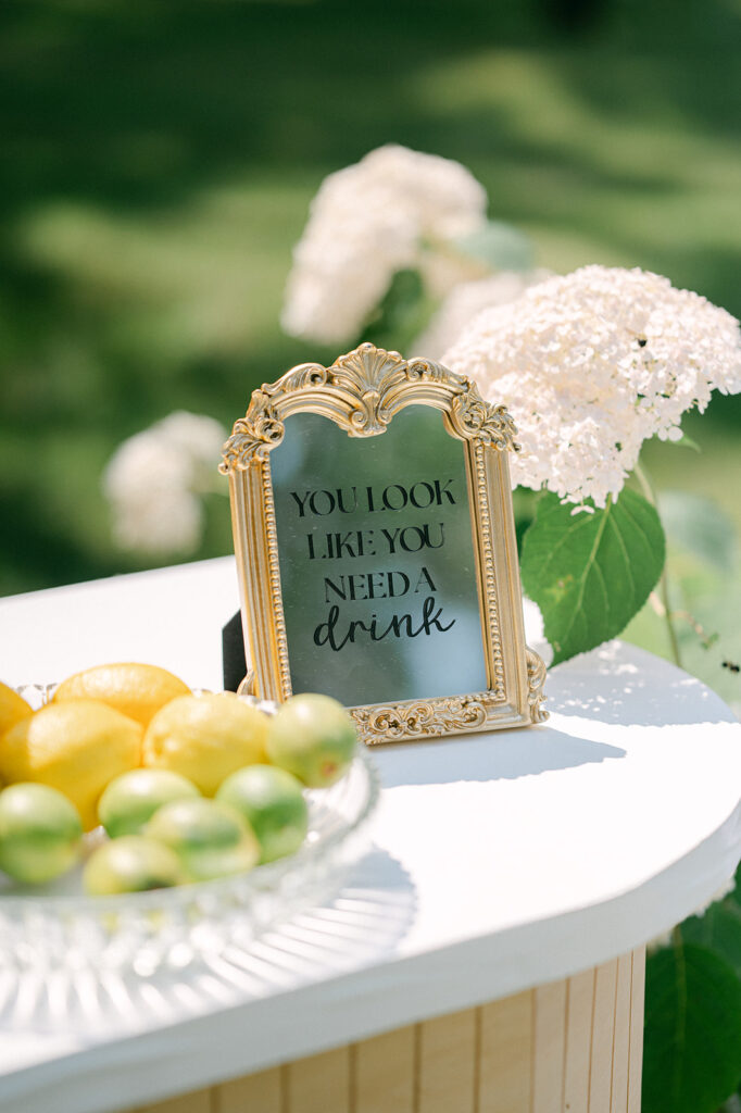 Gold framed mirror with black lettering that says, "you look like you need a drink" at a garden wedding in Minnesota. 