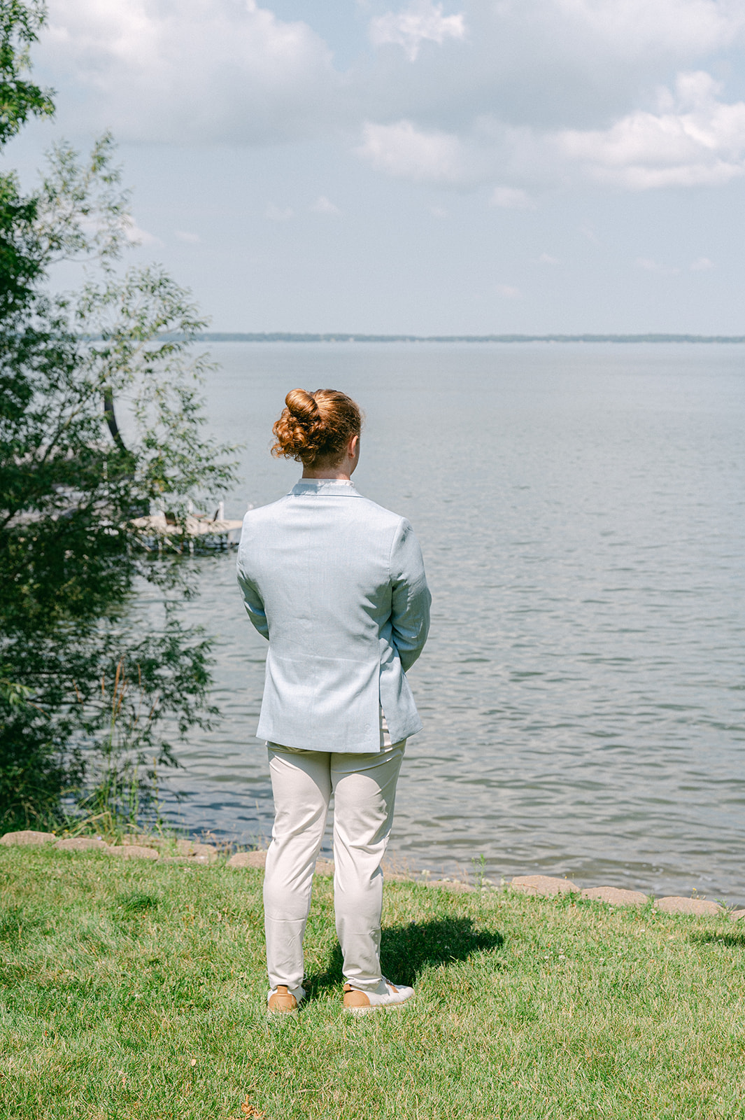 Groom standing by the lake, looking out in anticipation before the first look.