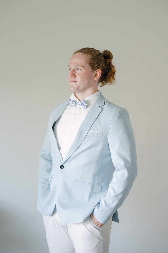 Whimsical garden party wedding groom portrait, featuring a light blue jacket and floral blue bowtie.