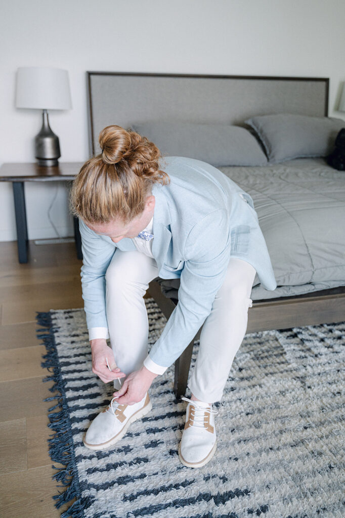 Groom sitting on a bed, putting on his shoes before a whimsical garden wedding.