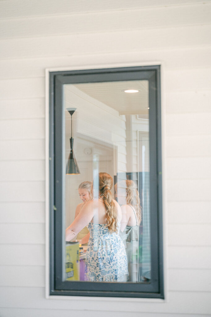 Documentary-style bridal party getting ready, captured from outside the house through a window. 