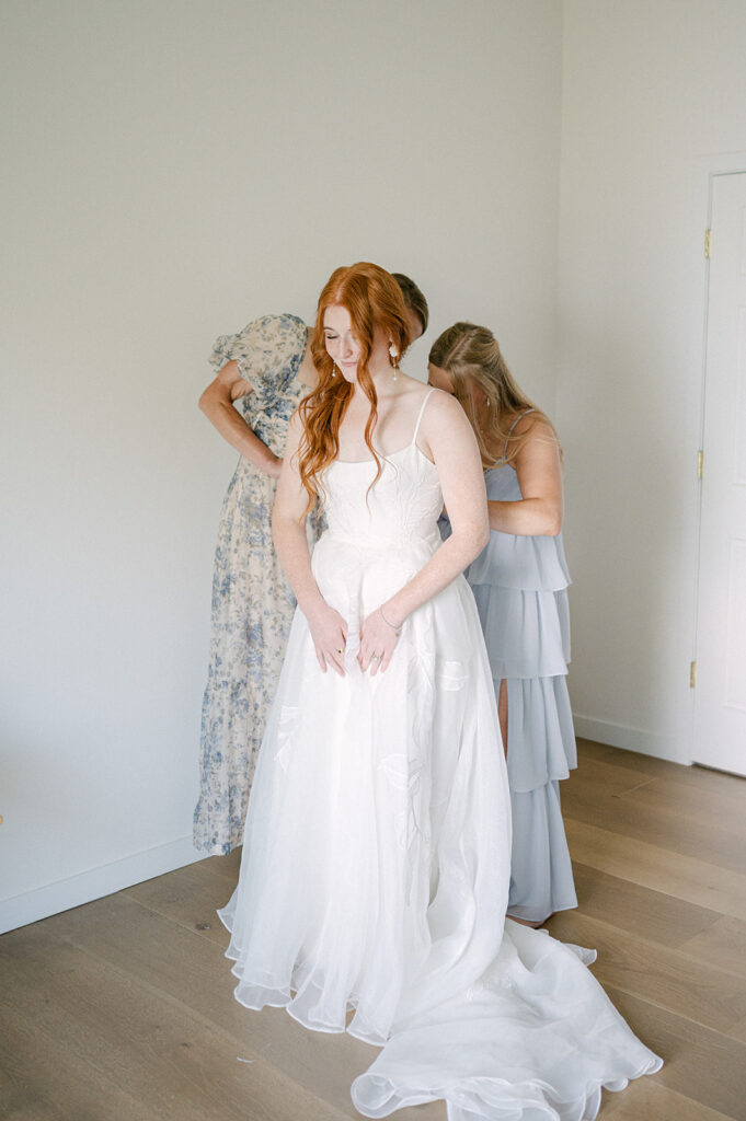 Candid moment of the bride as her mom and sister help zip up her wedding dress.