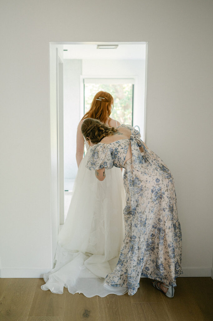 Editorial moment of the bride’s mom zipping up her wedding dress before the ceremony.